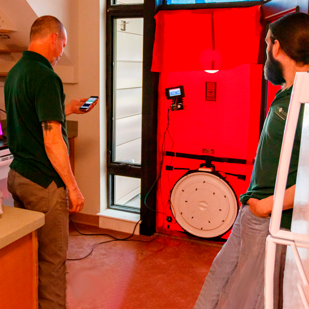2 men conducting a blower door test indoors, red vinyl sheathing suspended from doorway with blower fan at the bottom