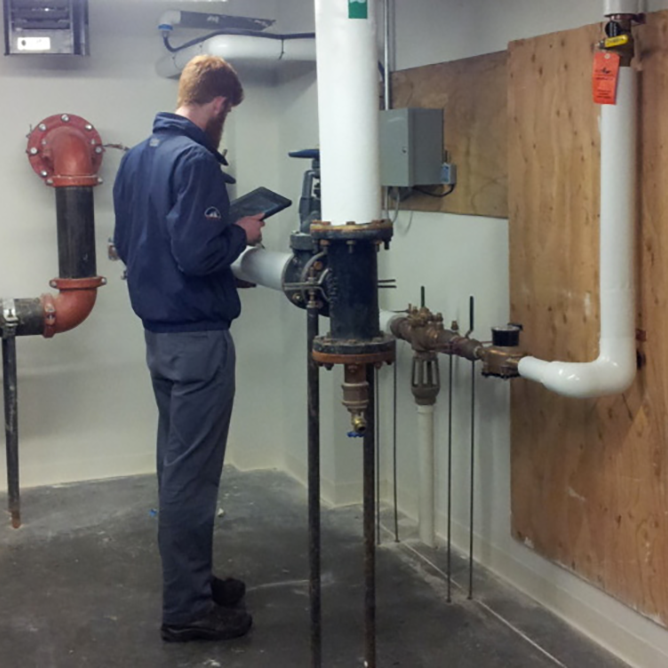 Image of an engineer in a boiler room assessing piping and equipment